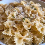 ['Close-up view of cooked bowtie pasta with a sprinkle of grated Parmesan cheese.', 'Side view of air-fried pasta, seasoned and garnished with herbs.', 'Juicy air-fryer pasta displayed on a plate, showcasing golden-brown edges.', 'Plate of al dente bowtie pasta tossed in olive oil, garlic, and spices.']