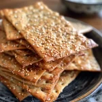['Close-up of crispy gluten-free crackers with a golden-brown hue and visible sesame and poppy seeds.', 'Side view of homemade gluten-free crackers featuring a crunchy texture and sprinkled toppings.', 'Detailed view of gluten-free crackers, highlighting their crispy edges and savory seasoning.', 'Freshly baked gluten-free crackers arranged neatly, showcasing a variety of seed toppings.']