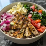 ['Close-up of a colorful Greek-style chicken protein bowl featuring chicken, quinoa, and fresh vegetables.', 'Side view of a Greek chicken protein bowl with vibrant ingredients arranged neatly in a bowl.', 'A delicious Greek chicken protein bowl filled with quinoa, diced tomatoes, cucumbers, and feta cheese.', 'Juicy Greek-style chicken protein bowl showcasing fresh veggies, chicken, and a drizzle of olive oil.']