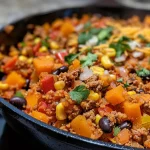 ['Close-up of a colorful Mexican Cauliflower Rice Skillet featuring diced bell peppers and ground beef.', 'A side view of a vibrant skillet filled with cauliflower rice, corn, and topped with shredded cheese.', 'Juicy Mexican Cauliflower Rice Skillet showing cubed butternut squash and black beans in a cast iron pan.', 'Appetizing image of a gluten-free dish with fresh ingredients like cilantro and taco seasoning in a skillet.']