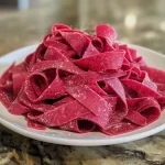 ['Close-up of vibrant homemade beet pasta, showcasing its rich red color and smooth texture.', 'Side view of freshly made beet pasta, with a glistening surface and intricate details.', 'A plate of beet pasta, highlighting its unique hue and fresh ingredients.', 'Juicy homemade beet pasta displayed on a wooden surface, emphasizing its artisanal quality.']