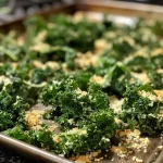 ['Close-up of crispy roasted kale leaves with a rich green color.', 'Side view of roasted Tuscan kale showing a textured surface and olive oil sheen.', 'Healthy roasted kale garnished with black pepper and garlic powder.', 'A vibrant pile of seasoned roasted kale leaves on a white plate.']