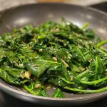 ['Close-up view of sautéed spinach with Parmesan cheese.', 'Side view of a vibrant green sautéed spinach dish glistening with olive oil.', 'Tasty sautéed spinach garnished with grated cheese and garlic salt.', 'Fresh spinach leaves sautéed in olive oil with a sprinkle of Parmesan.']