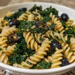 ['A close-up view of a plate of kale pasta with olives and garlic.', 'Side view of a serving of fusilli pasta topped with fresh kale and black olives.', 'Detailed shot showcasing kale pasta garnished with garlic and chili flakes.', 'A vibrant bowl of kale pasta featuring ingredients like olives and garlic.']