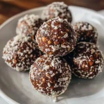['A close-up view of vegan gluten-free bliss balls, showcasing their rich texture and toppings.', 'Side perspective of delicious bliss balls made with dates, nuts, and cocoa, plated elegantly.', 'Juicy, round bliss balls in a natural setting, highlighting their ingredients like coconut and nuts.', 'A detailed shot of bliss balls stacked together, emphasizing their chocolatey exterior and toppings.']