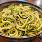 ['Close-up image of spiralized zucchini noodles drizzled with olive oil.', 'Side view photo of delicious zucchini noodles garnished with garlic and spices.', 'Juicy zucchini noodles with toppings displayed on a wooden surface.', 'Vibrant zucchini noodles styled with cherry tomatoes and herbs.']