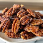 Close-up of shiny, candied pecans in a bowl, glistening with syrup.