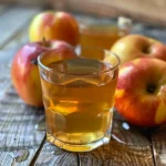 Close-up of a jar filled with apple cider vinegar and fresh apples beside it.