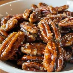 Close-up side view of shiny candied pecans on a white surface.