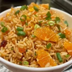 Close-up view of vibrant orange rice mixed with cranberries and garnished with green onions.