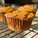 A close-up side view of golden-brown Sweet Potato Spice Muffins with a textured exterior.