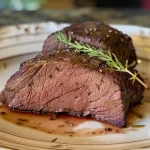 Close-up side view of a juicy venison tenderloin on a plate.