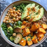 A close-up view of a warm ancient grain bowl filled with sweet potatoes, Brussels sprouts, chickpeas, and avocado.